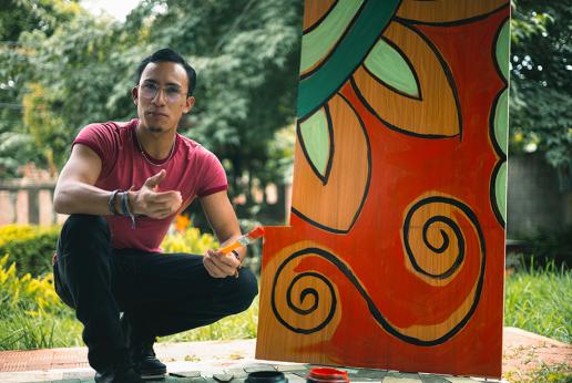 joven hombre agachado frente a una pintura de flor en estilo lenca posa para la fotografia.