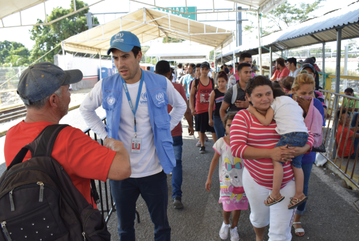 Persona de ACNUR dialoga con hombre en medio de fila en migración.