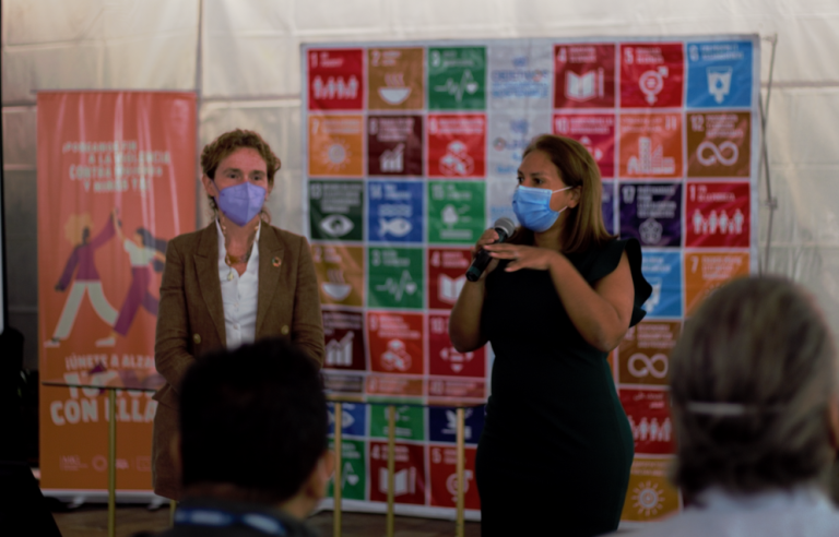 Coordinadora residente y representante de FAO ante auditorio de personas con un banner de los 17 objetivos de desarrollo sostenible y los 16 días de activismo detrás de ellas.